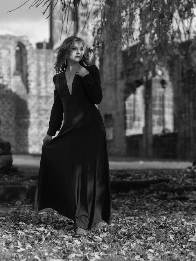 A long dark dress against ruined stone arches.