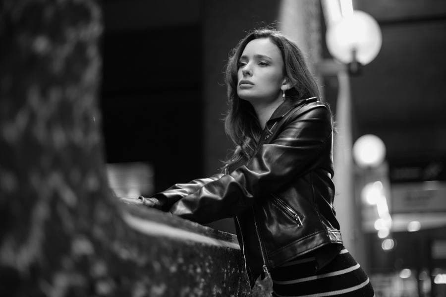 A figure leaning on a ledge, leather jacket, city light.